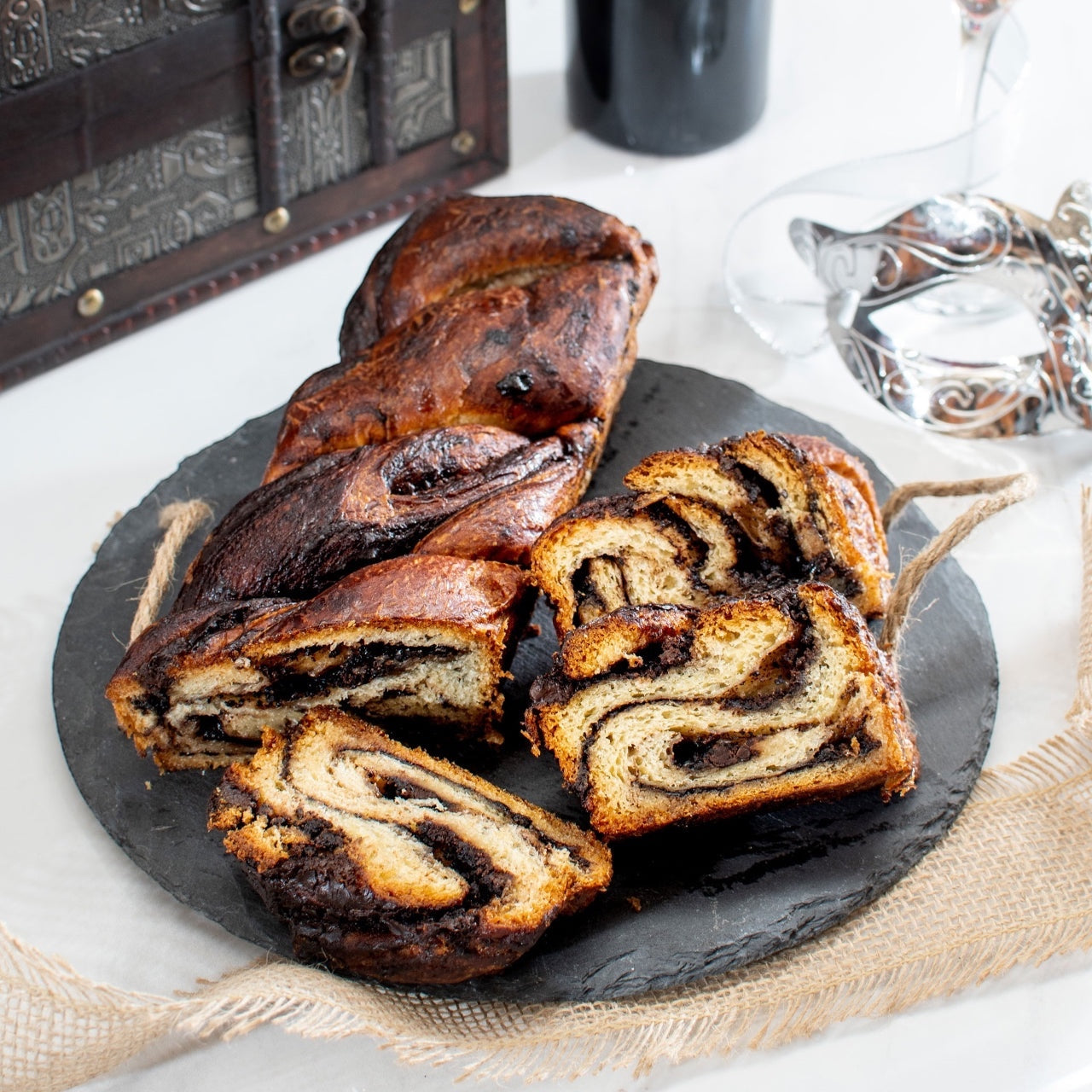 Kosherline gourmet chocolate babka cake sliced on a round slate board with a treasure chest gift box in the background