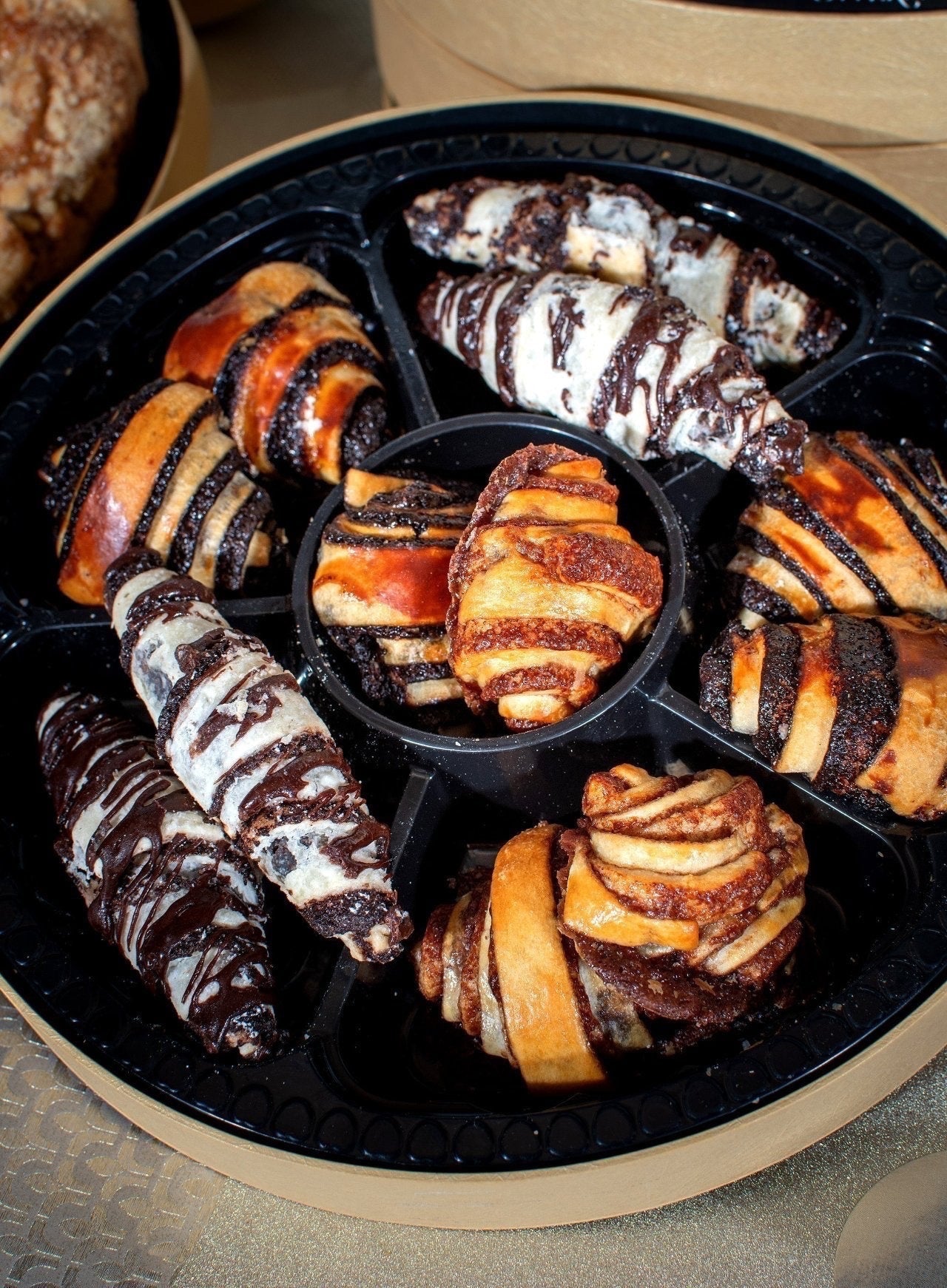 Kosherline gourmet pastry assortment featuring chocolate-drizzled rugelach and cinnamon swirls in a round gift tray