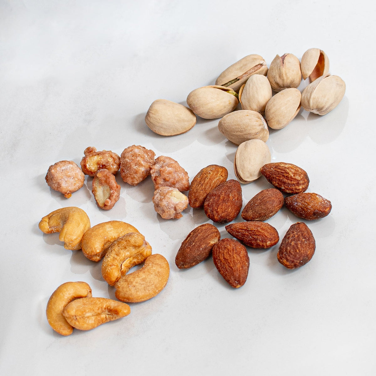 Kosherline gourmet assortment of roasted almonds, cashews, pistachios, and sugar-coated nuts on a marble surface.