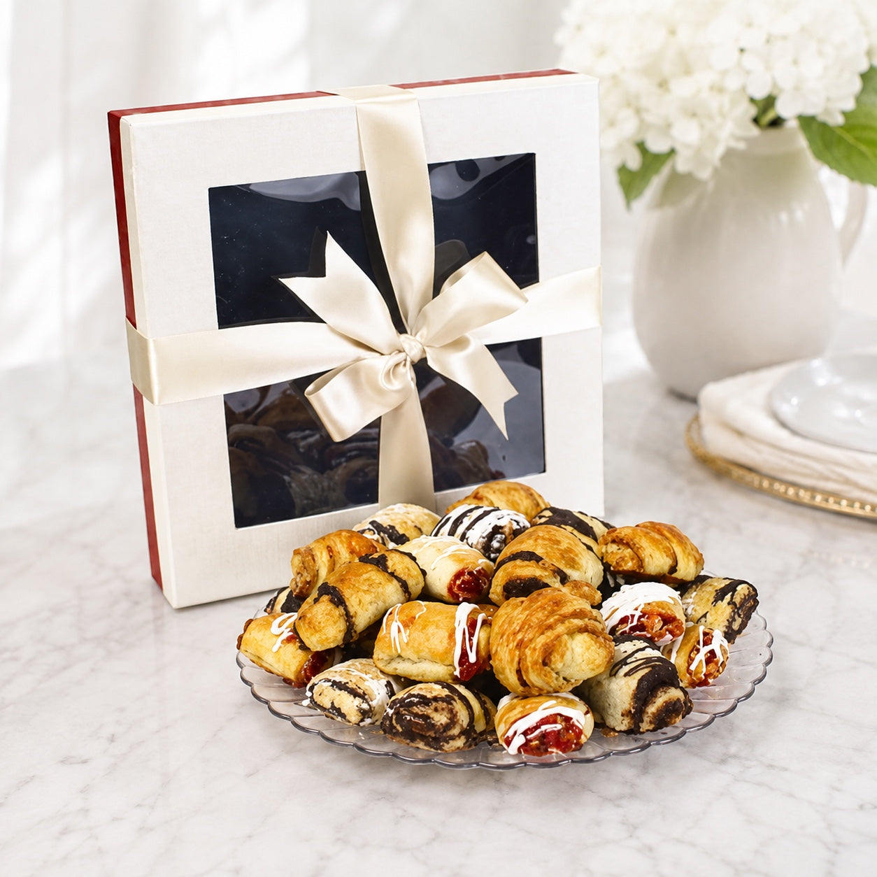 Kosherline assorted gourmet rugelach pastries with chocolate and cinnamon on a glass plate with a gift box.