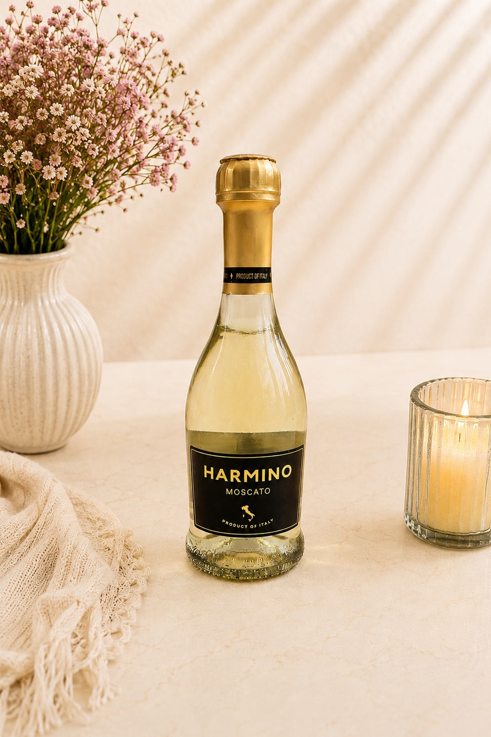 Kosherline Harmino Moscato sparkling wine bottle on a table with a vase of flowers and a lit candle