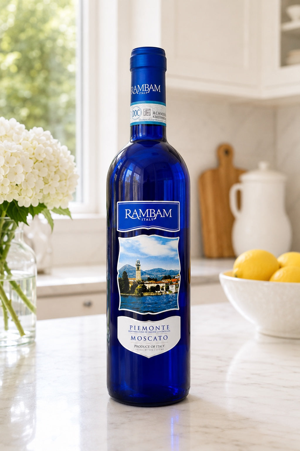 Kosherline Rambam Moscato wine bottle in a bright kitchen setting with white flowers and lemons