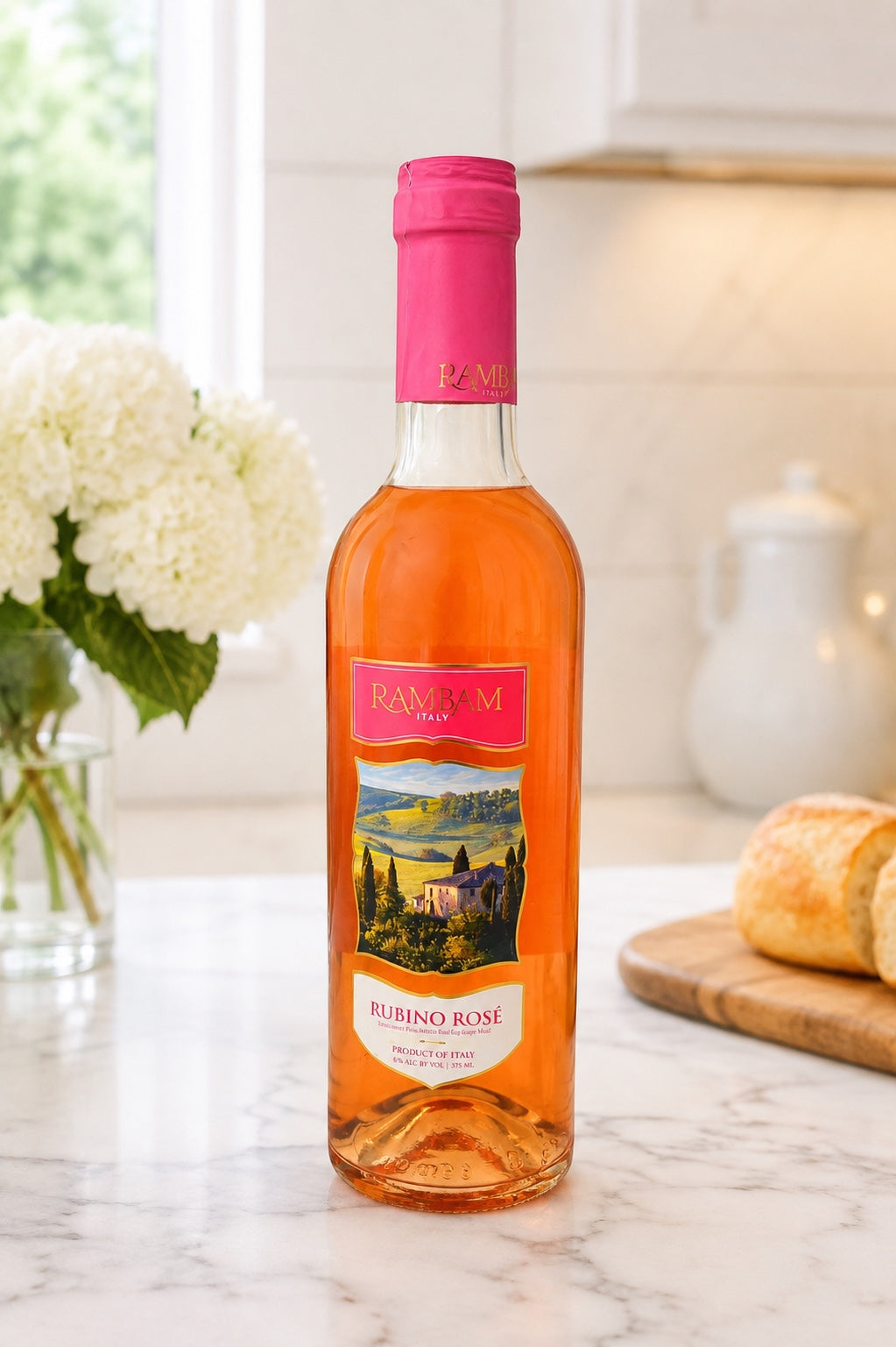 Kosherline Rambam Rubino Rose wine bottle with pink foil top on a marble kitchen counter with white flowers