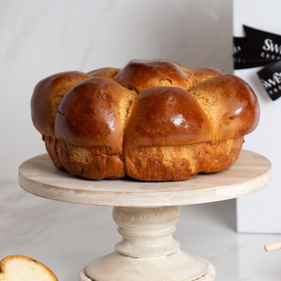 Kosherline gourmet round challah bread served on a rustic wooden cake stand for a festive holiday celebration