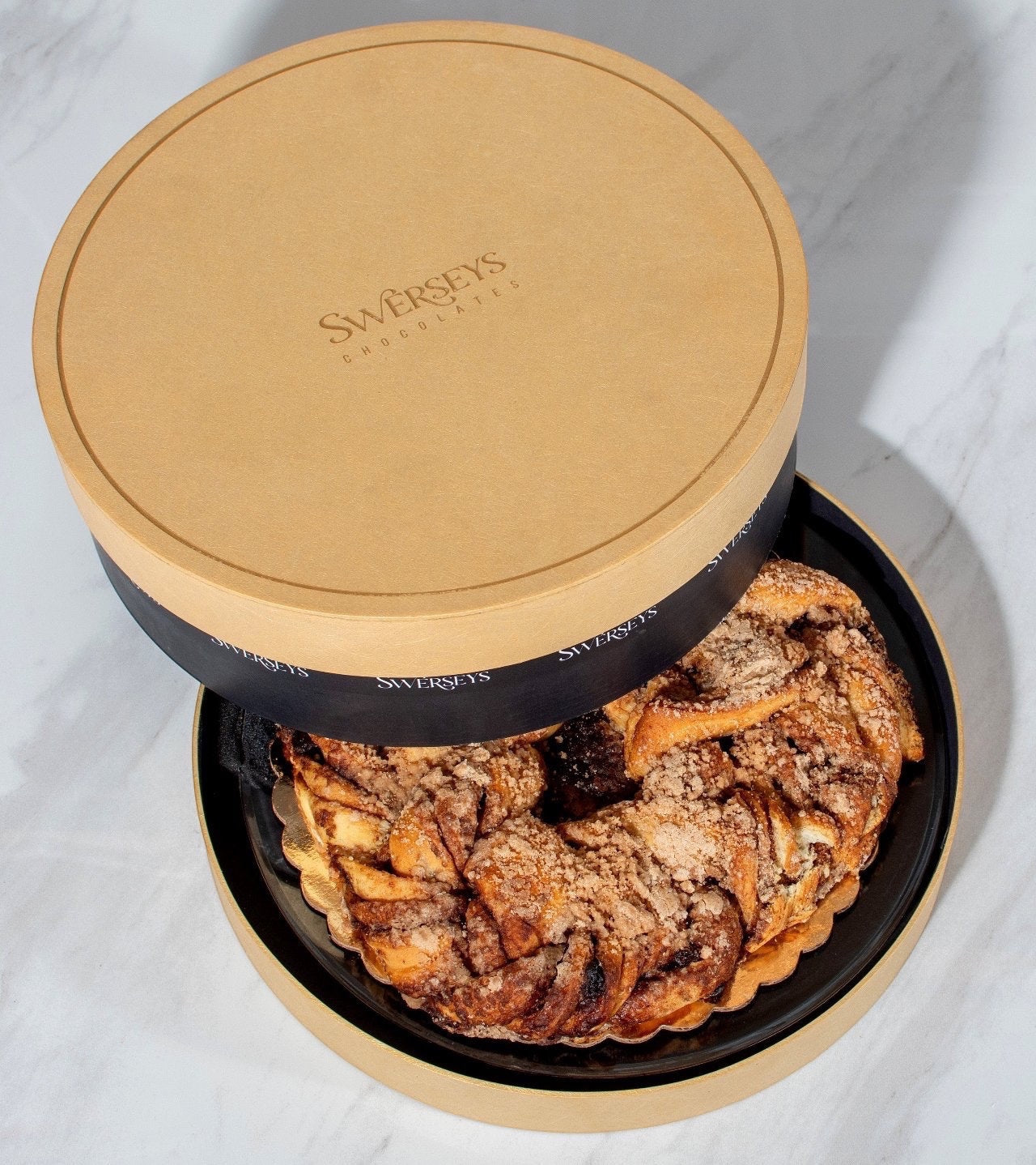 Kosherline Swerseys gourmet pastry in a round gold gift box with a crumb-topped bundt cake visible inside.