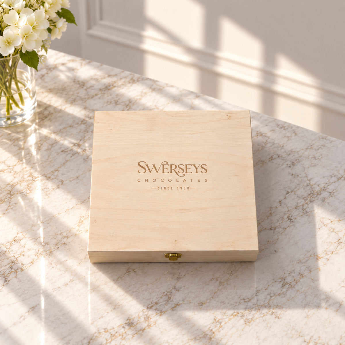 Kosherline small wooden gift box with Swerseys Chocolates branding, closed on a marble table with white flowers.