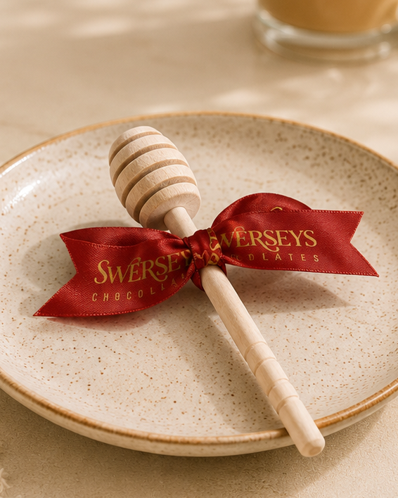Kosherline wooden honey dipper tied with a red ribbon on a speckled ceramic plate for Rosh Hashanah